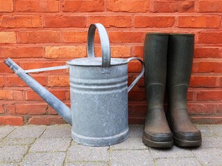 Zinc watering can and garden boots in front of a red brick wall. © nipa