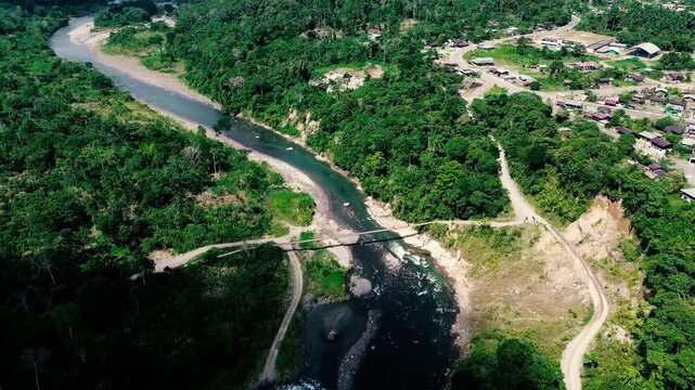 Drone footage looks across a small settlement in Ecuador&rsquo;s Oriente, with a grid of roads and scattered buildings bordered by dense tropical rainforest. A river curves through the foreground beneath fo