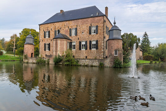 Kerkrade, Netherlands - Scenic Kasteel Erenstein castle reflected in moat pond with swimming ducks and a spurting water fountain.