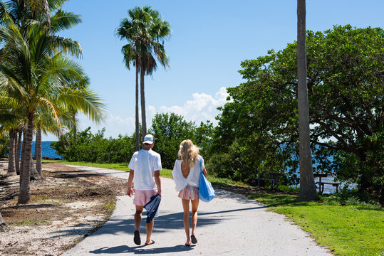 Couple Walking Through Tropical Waterfront Park on Sunny Day
