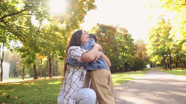 Mother reaches for son in autumn park while child shows reluctance toward physical affection. Scene suggests separation and sensory boundaries.
