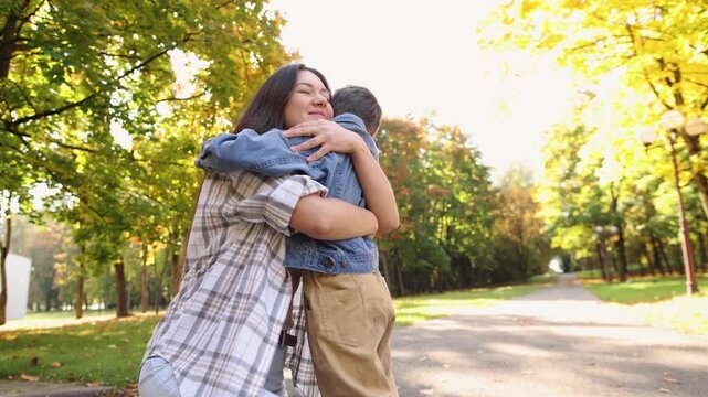 Mother embraces son despite his reluctance to cuddle during sunny autumn outing. Emotional scene explores different needs for physical affection within family.