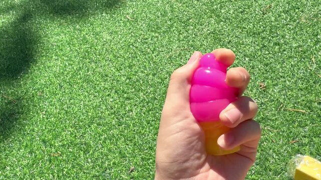 4K video of a hand holding a colorful ice cream shaped squishy stress relief toy outdoors. Bright sensory fidget toy for squeezing, relaxation, tactile play and entertainment.
