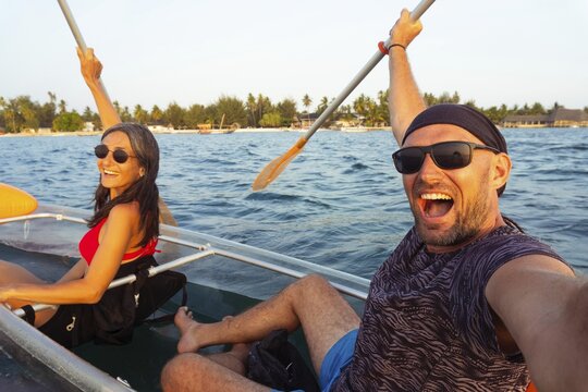 Happy casual couple cheers during a sunset clear kayak tour in Zanzibar. Point-of-view selfie capturing authentic joy, adventure, and tropical island vibes. Man woman bonding while travel together