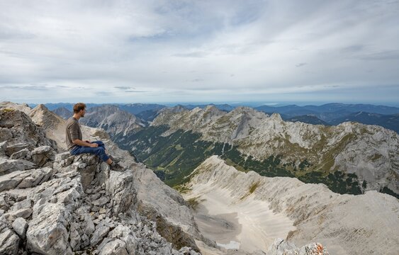 Hiker sitting at the summit of the Birkkarspitze, view of the Schlauchkar and Karwendeltal with the eastern Karwendelspitze, Hinterautal-Vomper chain, Karwendel, Tyrol, Austria
