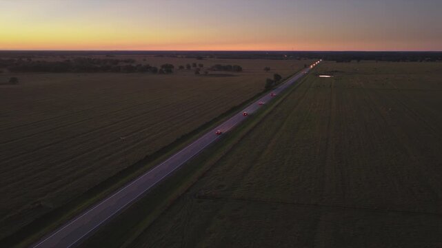 Quiet countryside highway with sparse traffic, glowing lights and dark surroundings, expressing calm, distance and late evening travel mood.