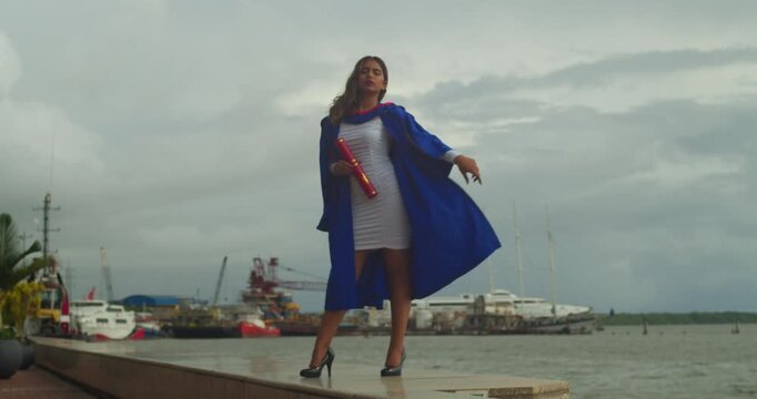 Academic achievement concept featuring a young female graduate looking at the camera in open air.