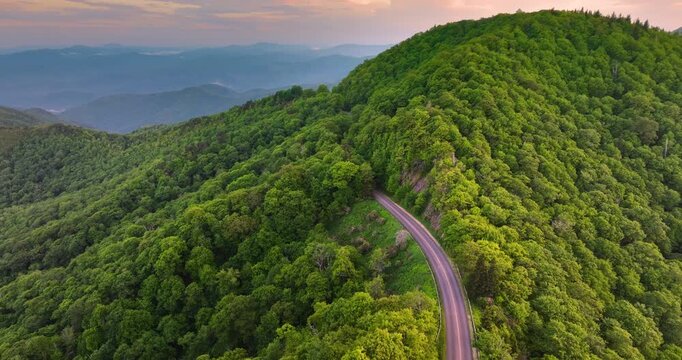Road trip driving in North Carolina Appalachian mountains at sunset. Winding parkway in mountain forest with green canopies in summer season