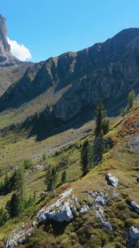 Vertical video, aerial  view across the green Mondeval alpine basin toward the massive rock walls of Lastoi de Formin near Passo Giau in the Italian Dolomites.