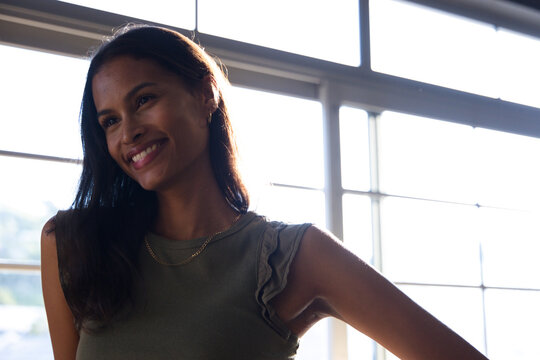 African American woman standing and smiling by mullioned window wearing olive top, gold chain