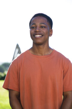 African American man smiling standing in sunlit park, wearing orange tee and hoop earring
