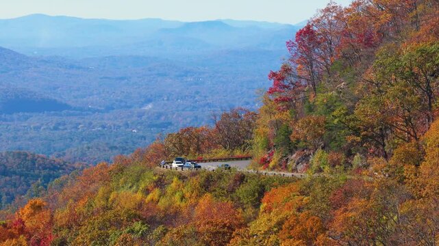 Scenic overlook in the Appalachian Mountains of Tennessee with a parked car enjoying breathtaking views of colorful autumn forest and rolling hills.