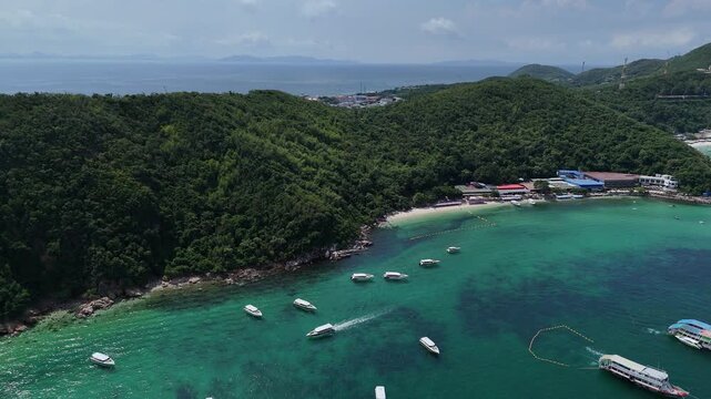 Scenic aerial view ascending over the emerald turquoise bay of Koh Larn island in Pattaya Thailand featuring white speedboats anchored near sandy beaches and lush green tropical hills under a blue sky