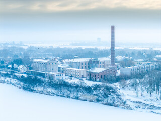 Widok z lotu ptaka na zabytkowe budynki przemysłowe z ceglanym kominem nad zaśnieżonym brzegiem rzeki w Opolu. Mglista, chłodna zima nadaje scenie spokojny, nostalgiczny charakter.  © Henryk Niestrój
