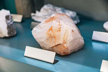 Fototapeta premium Displayed on a museum shelf, a large raw quartz specimen sits beside blank identification placards and other minerals.