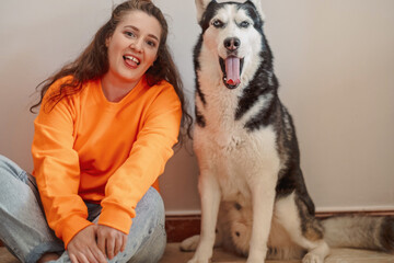 Young woman and Siberian husky sitting together on warm floor, pose nobody had to teach them, friendship without any condition. Wide shot. Concept of time spent together with own northern dog © iwavephoto