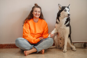 Young woman and Siberian husky sitting together on warm floor, pose nobody had to teach them, moment without any command. Wide shot. Concept of time spent together with own northern dog © iwavephoto