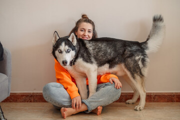 Young woman embracing Siberian husky standing on floor, arms wrapped around whole animal, warmth passed without words. Wide shot. Concept of embracing dog as sign of real affection © iwavephoto