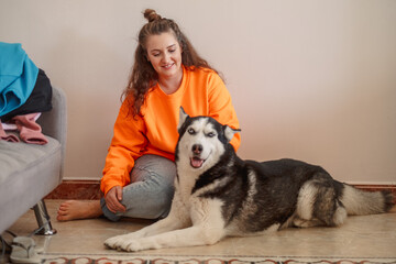 Young woman stroking Siberian husky lying on warm floor, hand resting on warm thick fur, image made for honest content marketing. Wide shot. Concept of stroking dog as daily sign of real care © iwavephoto