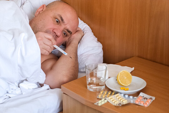 Sick middle aged man with fever lying on bed and staring at thermometer in fright. Flu, illness, virus, cold symptom and health care concept