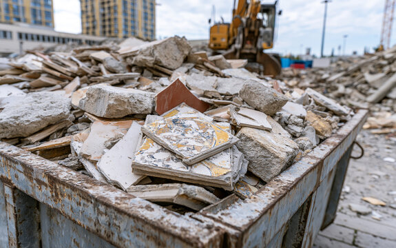Construction debris in metal container. Broken tiles and concrete rubble. Renovation waste pile. Demolition materials and discarded fragments. Urban cleanup area