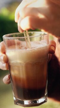 Close-up of a woman stirring a homemade pumpkin spice latte as creamy pumpkin and milk swirl into dark coffee. Warm autumn sunlight creates beautiful reflections on the glass