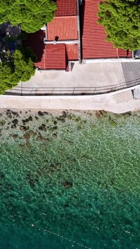 Croatia, aerial top down view of a coastal house with red tile roof, turquoise sea water and rocks, drone footage
