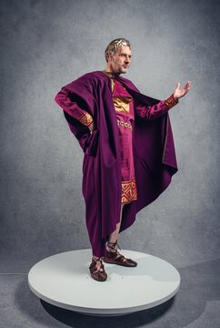 Man in ancient Roman-style ceremonial robe gesturing on a studio platform, concept of ancient religion