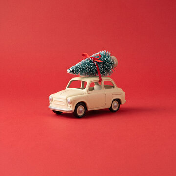 Retro cream toy car with miniature Christmas tree, festive holiday vehicle on red background, winter seasonal delivery concept for greeting cards