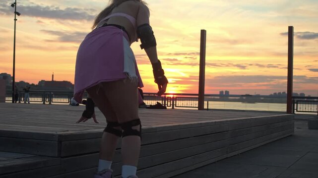 Female skater arrives at wooden deck grabbing phone from waist bag. She sits down relaxing against bright summer sunset while scrolling social media feed after intense outdoor rollerblading workout.