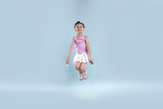 Cute little girl jumping with skipping rope on light blue background