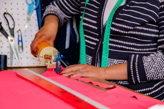A woman's hand cutting fabric with a cutting machine after making marks - work concept
