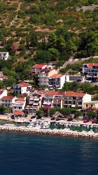 Croatia, aerial footage of a coastal village with traditional houses, marina with boats, and lush green hills