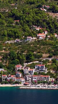Croatia, aerial view of coastal village with red roof houses, green hills, and sea