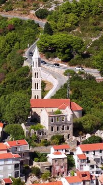 Croatia, aerial view of a winding road through a green forest and traditional coastal village with red rooftops