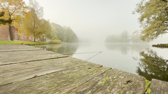 A wooden dock extends over a calm lake shrouded in mist. The autumn landscape evokes a peaceful and nostalgic mood. This quiet scene rests in Catherine Park, Pushkin, Saint Petersburg.