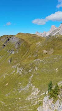 Vertical video, aerial  view across the green Mondeval alpine basin toward the massive rock walls of Lastoi de Formin near Passo Giau in the Italian Dolomites.