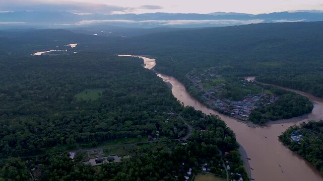 A broad river curves through an expansive tropical forest canopy, with pale sandbars along its banks and a few scattered buildings visible at the forest edge. Aerial drone footage filmed near Misahual