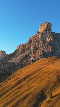 Vertical video,  aerial view of  Ra Gusela rising above grassy alpine slopes and a mountain hut at Passo Giau in the Dolomites, Italy, supporting themes of hiking, mountain travel and outdoor. 