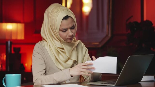 Young Muslim businesswoman opening envelope and reading letter at work