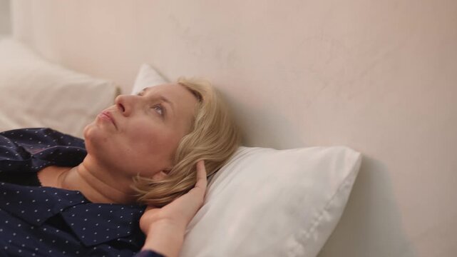 Tired woman in her 50s has headache while lying in bed after poor sleep