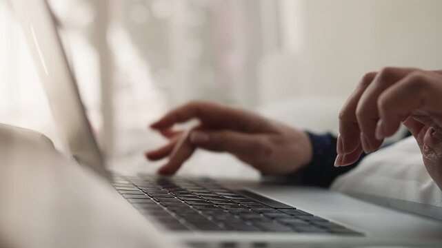 Close-up of female freelancer typing on laptop while working remotely in bed