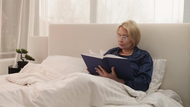 Middle-aged woman reads a book while lying in bed, enjoying a quiet hobby