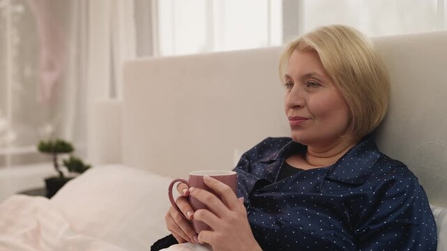 Woman in her 50s enjoys coffee in bed after restful sleep, morning routine