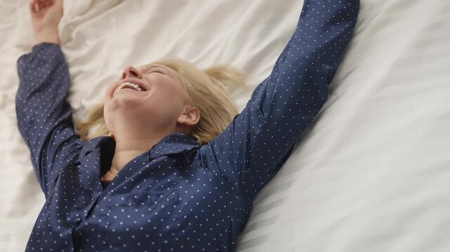 Happy middle-aged woman falls onto soft bed smiling, enjoying time to relax