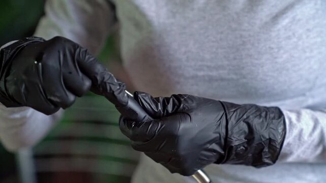 Close-up of gloved hands inserting metal drill bit into handheld rotary tool showing precise assembly motion and protective nitrile gloves in soft natural light
