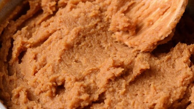 A wooden spoon spreads shiro miso paste in macro view, revealing its thick, grainy consistency.