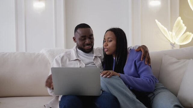 Young African American couple booking cinema tickets online using laptop