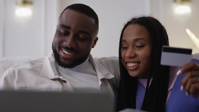 Young African American couple use credit card to make payment on laptop