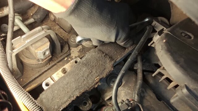 A car mechanic in black gloves uses an open-end wrench to turn a bolt inside the engine compartment during vehicle repair, close-up.